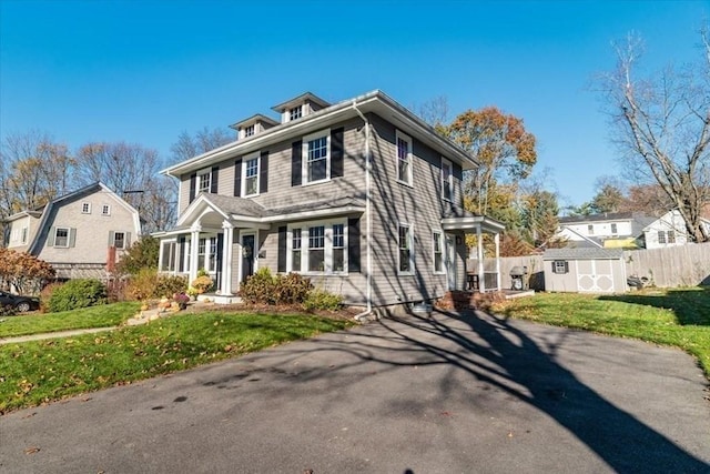 american foursquare style home with a shed, a front yard, fence, and an outbuilding