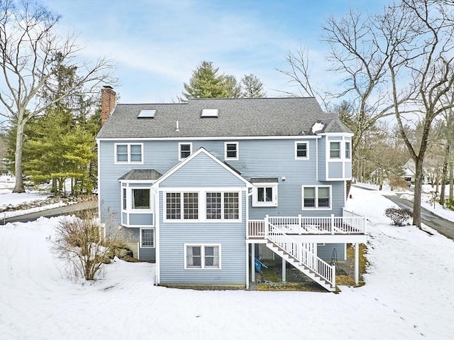 snow covered rear of property with stairs, a chimney, a deck, and roof with shingles