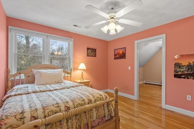 bedroom featuring baseboard heating, light wood-type flooring, visible vents, and baseboards