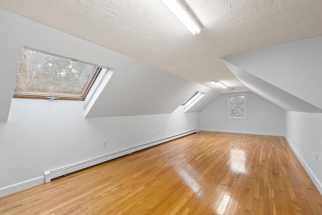 additional living space with baseboards, lofted ceiling, hardwood / wood-style flooring, a textured ceiling, and a baseboard heating unit