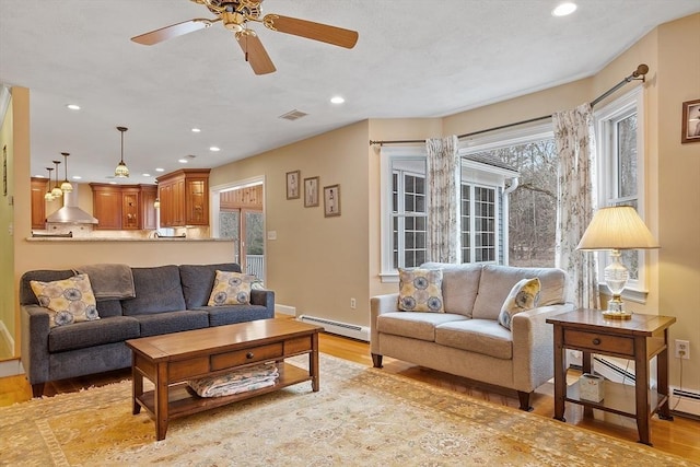 living area with a baseboard heating unit, light wood-type flooring, visible vents, and recessed lighting