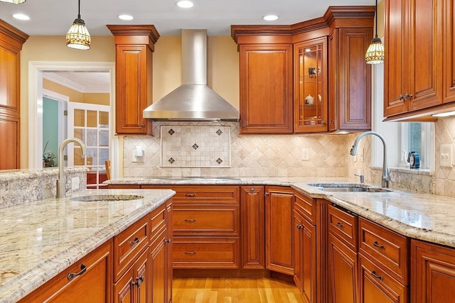 kitchen featuring wall chimney exhaust hood, hanging light fixtures, a sink, and light stone countertops