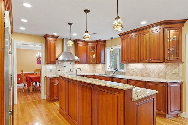 kitchen featuring light stone counters, a sink, light wood-style flooring, and wall chimney exhaust hood