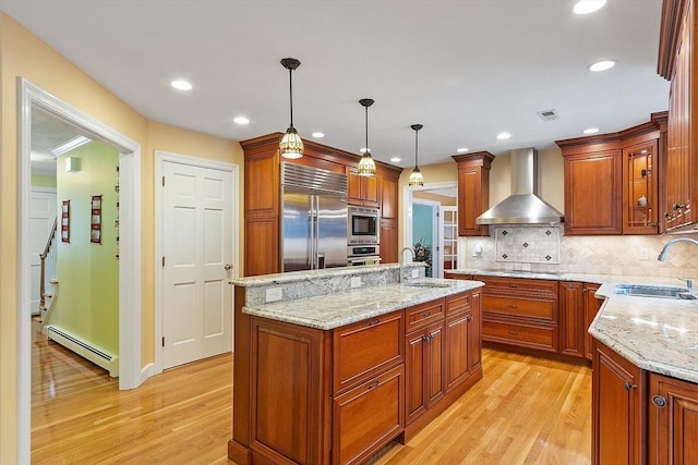 kitchen with a baseboard radiator, wall chimney exhaust hood, a sink, and built in appliances