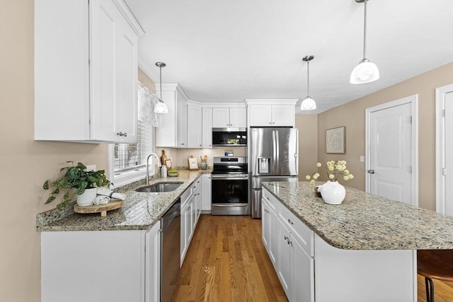 kitchen featuring sink, white cabinetry, a center island, hanging light fixtures, and stainless steel appliances