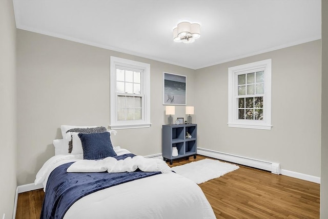 bedroom with crown molding, wood-type flooring, and a baseboard heating unit