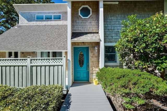 property entrance with roof with shingles and fence