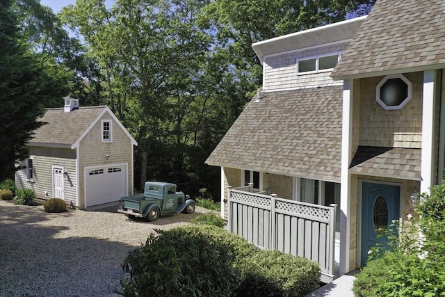 view of home's exterior featuring an outdoor structure, driveway, a shingled roof, and a garage