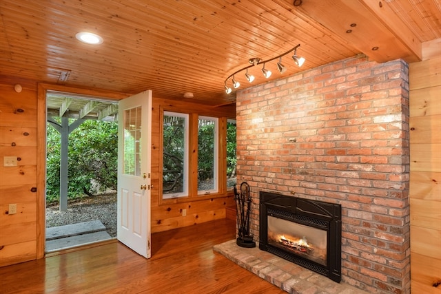 unfurnished living room with a healthy amount of sunlight, hardwood / wood-style floors, a brick fireplace, and wooden walls