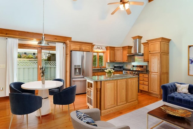 kitchen featuring a center island, wall chimney range hood, light wood finished floors, stainless steel appliances, and high vaulted ceiling