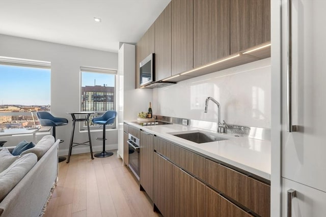 kitchen with black electric stovetop, oven, light hardwood / wood-style flooring, and sink