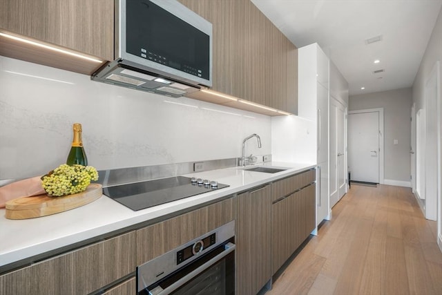 kitchen with light wood-type flooring, black electric cooktop, oven, and sink