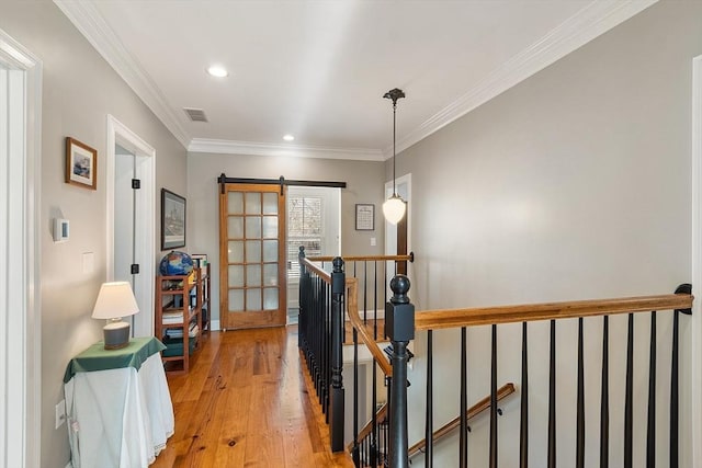 corridor with visible vents, an upstairs landing, a barn door, light wood-style floors, and crown molding