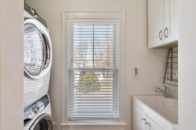 laundry area featuring stacked washer and dryer, cabinet space, and a sink