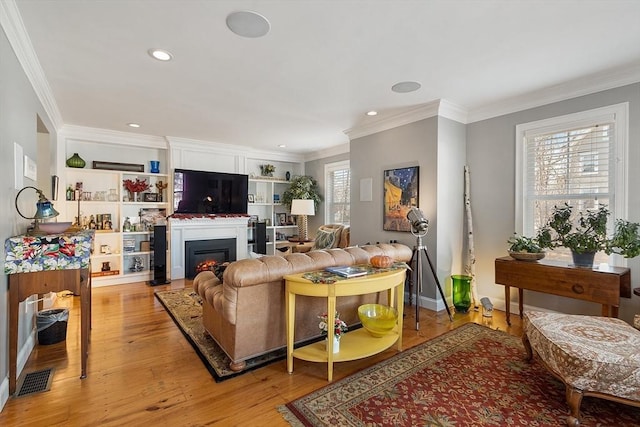 living room featuring light wood-style flooring, a warm lit fireplace, and ornamental molding