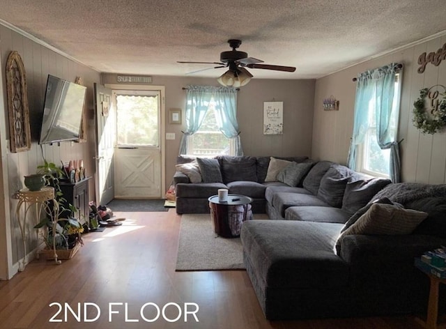 living room with ceiling fan, wooden walls, a textured ceiling, and hardwood / wood-style floors