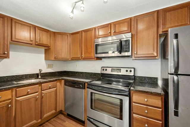 kitchen featuring light wood-type flooring, stainless steel appliances, sink, and dark stone counters