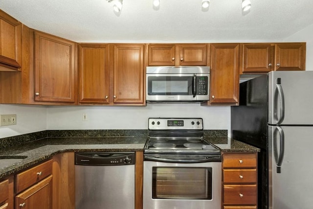 kitchen with dark stone countertops, a textured ceiling, and appliances with stainless steel finishes