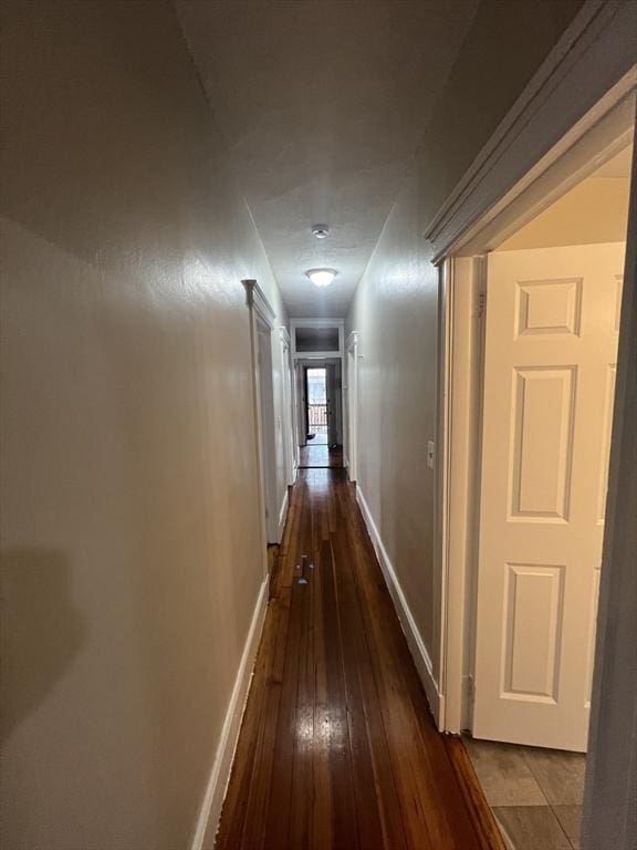 hallway featuring dark wood-type flooring and baseboards