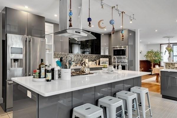 kitchen with appliances with stainless steel finishes, tasteful backsplash, island exhaust hood, a breakfast bar, and a spacious island