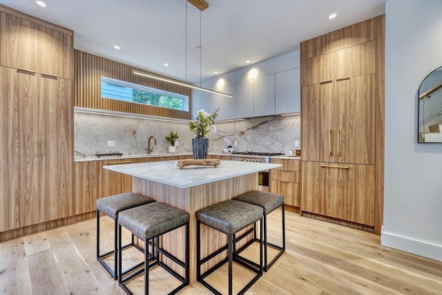 kitchen with backsplash, light hardwood / wood-style floors, a kitchen island, sink, and a kitchen breakfast bar