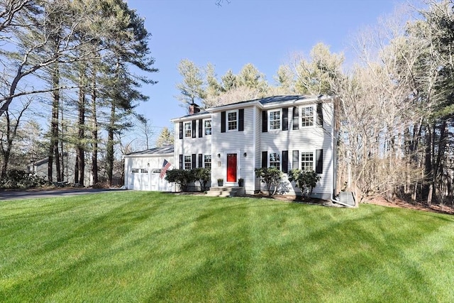 colonial inspired home with a chimney, an attached garage, entry steps, driveway, and a front lawn