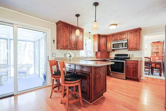 kitchen with a peninsula, a breakfast bar, light wood-style floors, appliances with stainless steel finishes, and decorative light fixtures