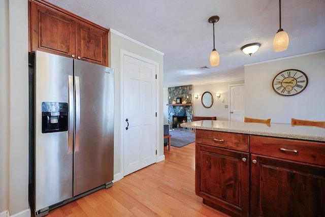 kitchen featuring a stone fireplace, light wood-style floors, stainless steel fridge, decorative light fixtures, and crown molding