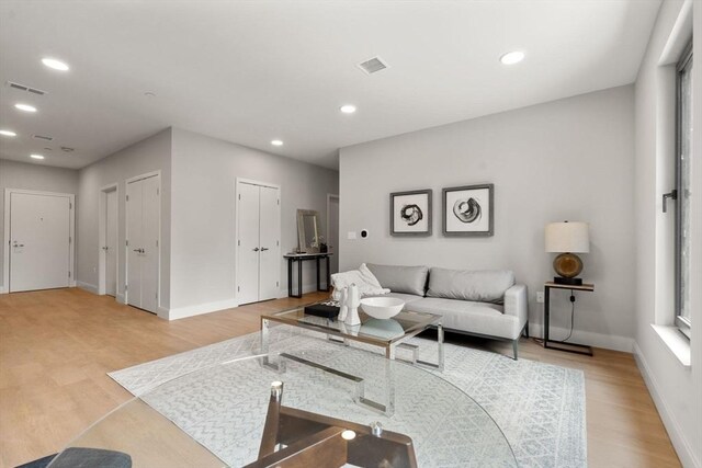 living area featuring visible vents, light wood-style floors, and baseboards