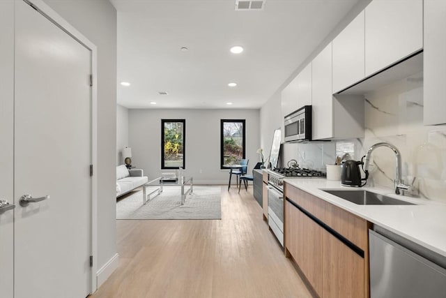 kitchen featuring recessed lighting, light countertops, a sink, light wood finished floors, and stainless steel appliances