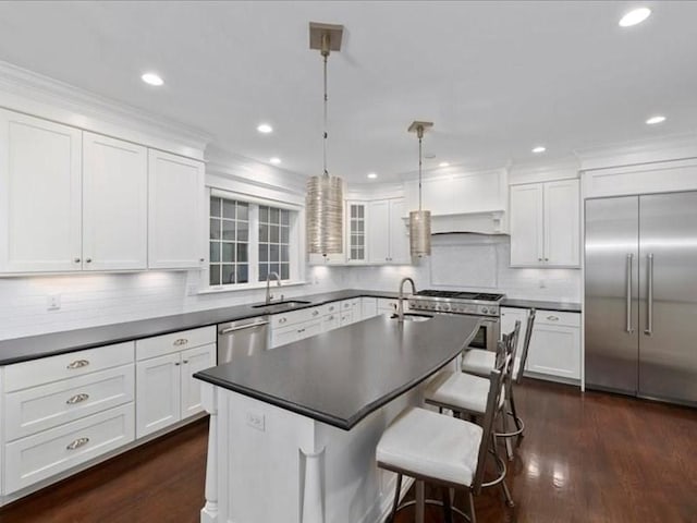 kitchen featuring white cabinets, high quality appliances, hanging light fixtures, and an island with sink