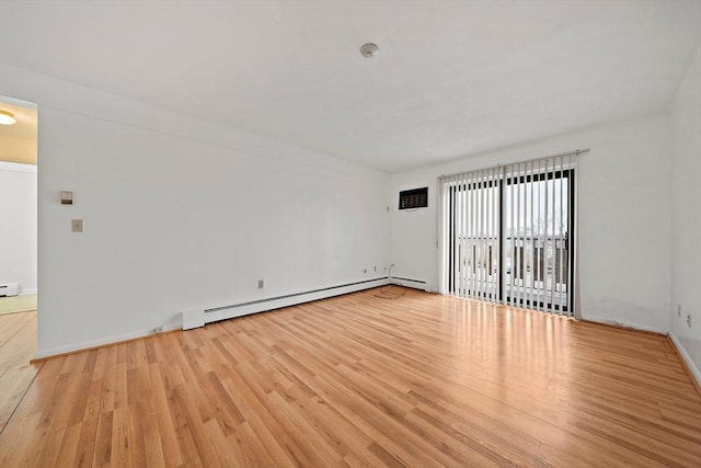 spare room featuring a baseboard heating unit, baseboards, and wood finished floors