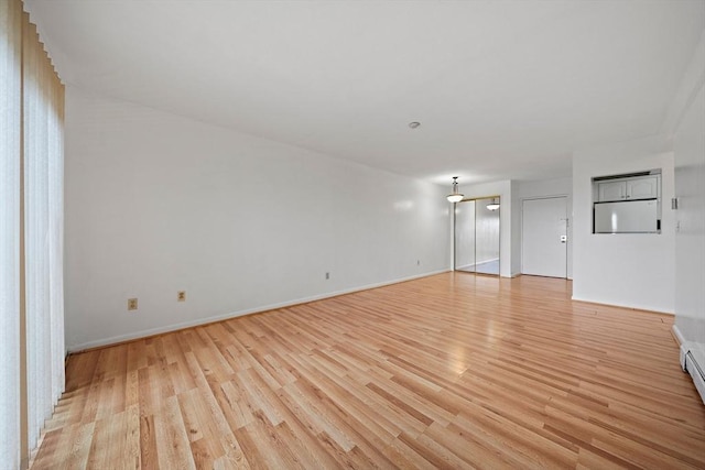 unfurnished room featuring baseboard heating, light wood-type flooring, and baseboards