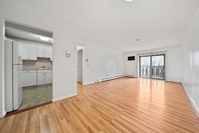 unfurnished living room with a sink, a baseboard heating unit, baseboards, and light wood finished floors