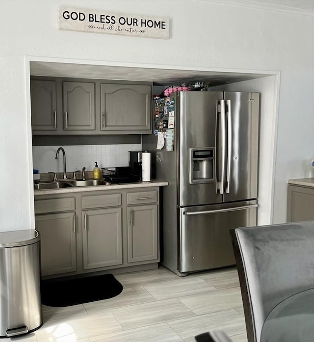 kitchen with gray cabinets, tasteful backsplash, sink, and stainless steel fridge