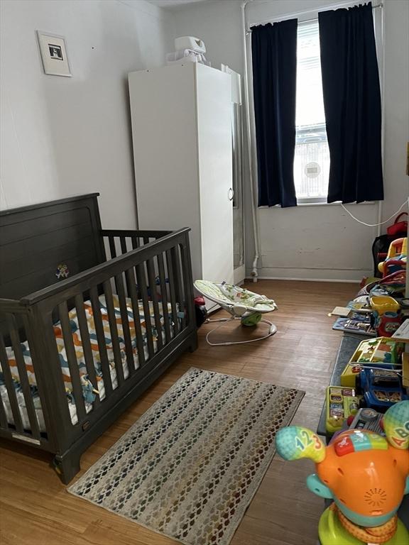 bedroom featuring a nursery area, wood-type flooring, and cooling unit