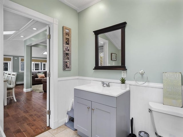 half bathroom with vanity, ornamental molding, baseboard heating, and a wainscoted wall