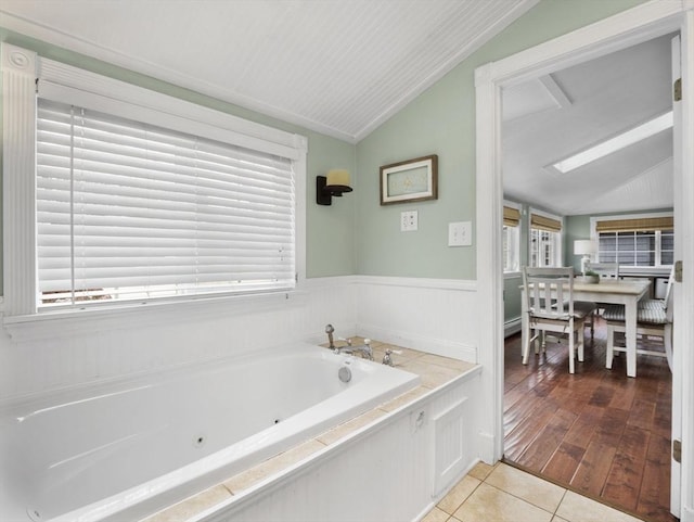 full bathroom with tile patterned floors, vaulted ceiling, a tub with jets, and a wainscoted wall