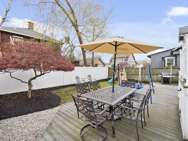 wooden terrace with a fenced backyard, outdoor dining area, a playground, and area for grilling