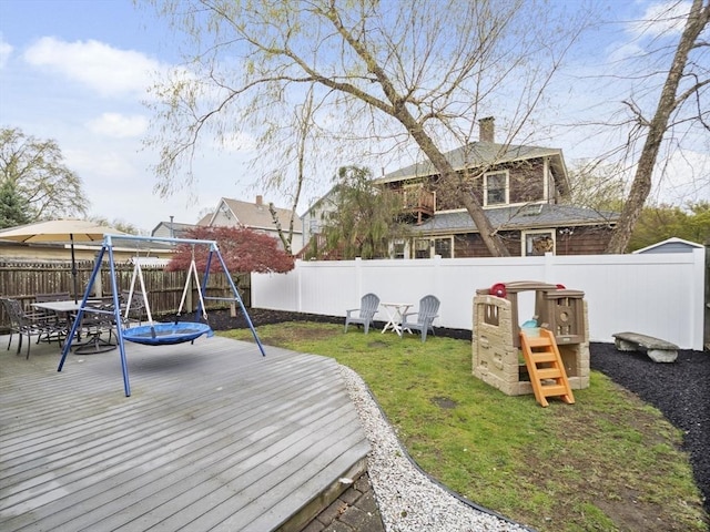 view of yard featuring outdoor dining area, a fenced backyard, a playground, and a deck