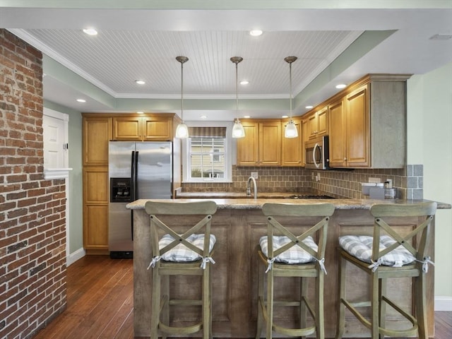 kitchen with light stone counters, a peninsula, appliances with stainless steel finishes, and dark wood-style floors