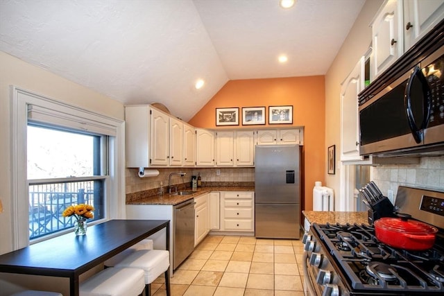 kitchen with appliances with stainless steel finishes, white cabinetry, sink, vaulted ceiling, and light tile patterned floors