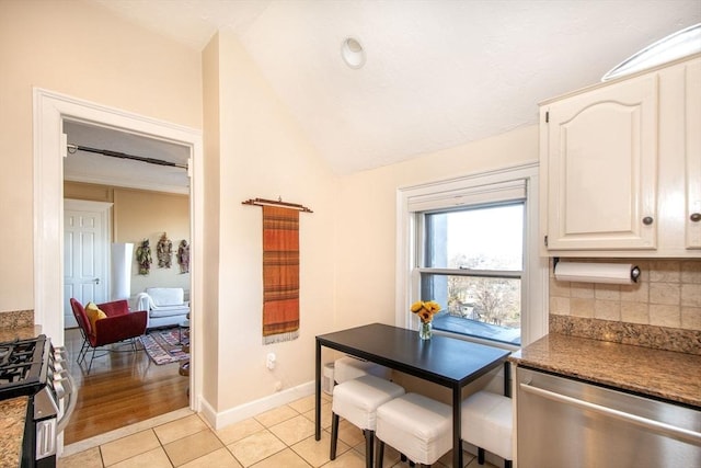 kitchen featuring appliances with stainless steel finishes, lofted ceiling, white cabinetry, tasteful backsplash, and light tile patterned floors