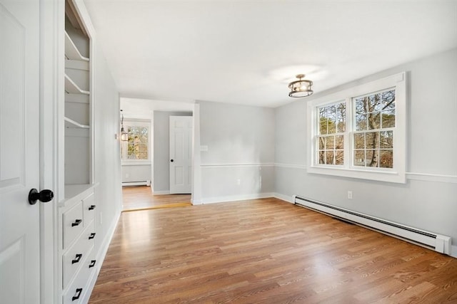 empty room with a chandelier, a baseboard radiator, and light hardwood / wood-style floors