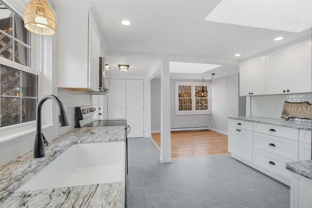 kitchen with a skylight, tasteful backsplash, stainless steel appliances, a baseboard heating unit, and white cabinets