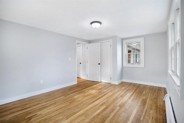 unfurnished bedroom with light hardwood / wood-style flooring, a closet, and a baseboard heating unit