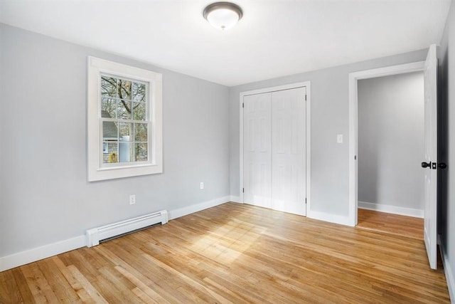 unfurnished bedroom featuring hardwood / wood-style floors, a closet, and baseboard heating