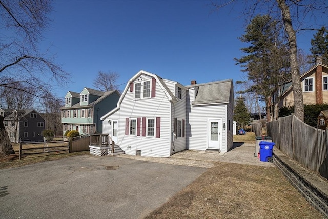 back of house with a gambrel roof, driveway, a shingled roof, and fence