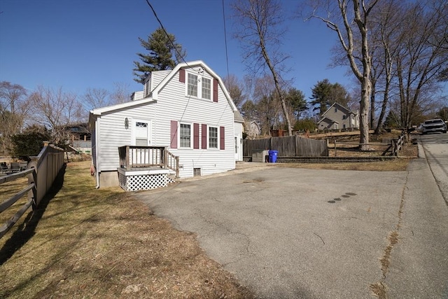 back of house with crawl space, aphalt driveway, a gambrel roof, and fence