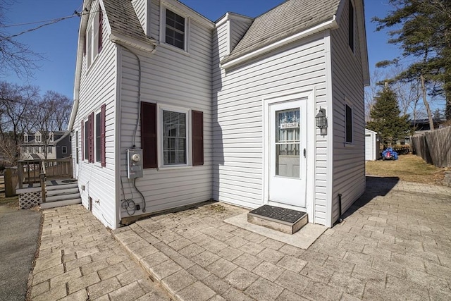 rear view of house featuring a deck, a patio area, fence, and roof with shingles